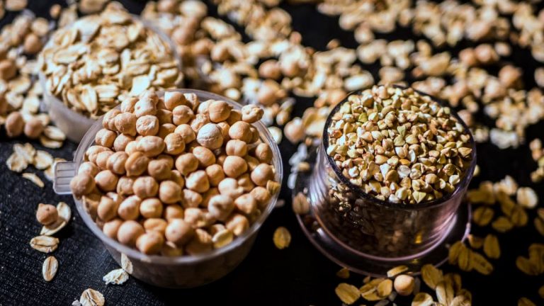 Close-up of assorted raw grains and seeds in cups on a dark background, showcasing variety and texture.